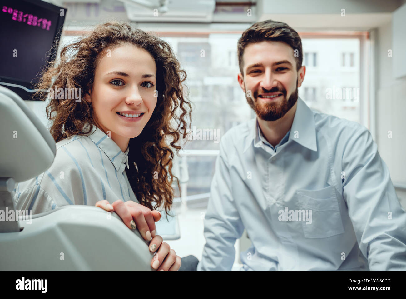 Ritratto di una donna con sorriso toothy seduto alla poltrona odontoiatrica con medico sullo sfondo presso lo studio dentistico. Foto Stock