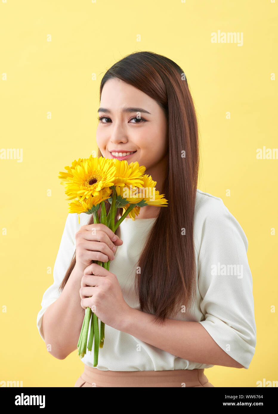 Giovane donna odore di girasoli su sfondo giallo Foto Stock