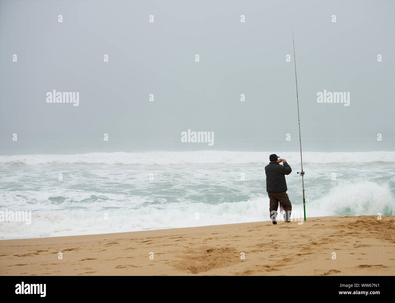 L'uomo con la canna da pesca sulla spiaggia, il mare, le onde, schiuma, wind surf, Foto Stock