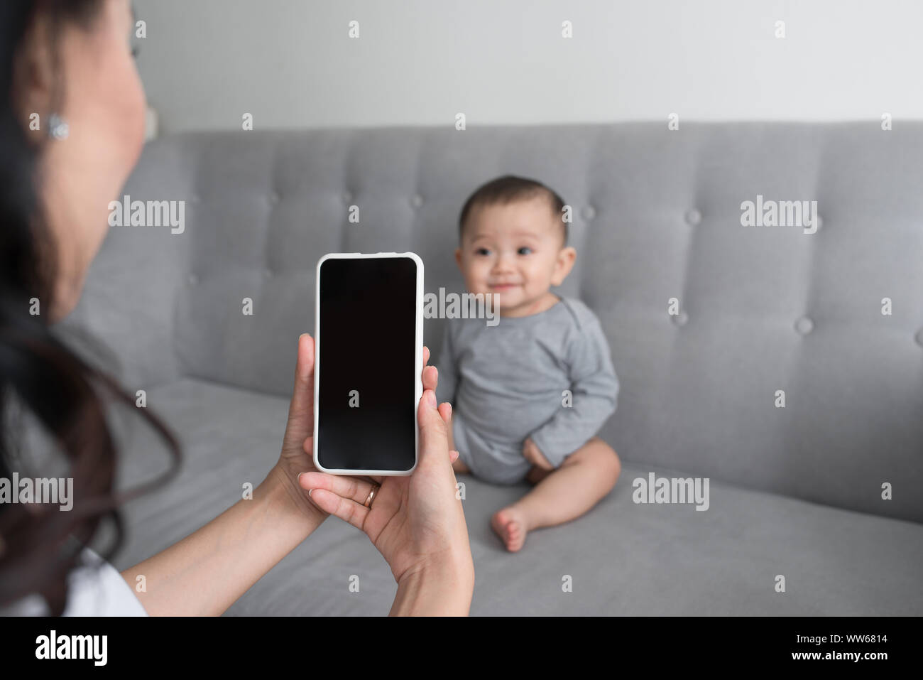 Felice madre di scattare una foto della sua bambina sul divano con smart phone Foto Stock