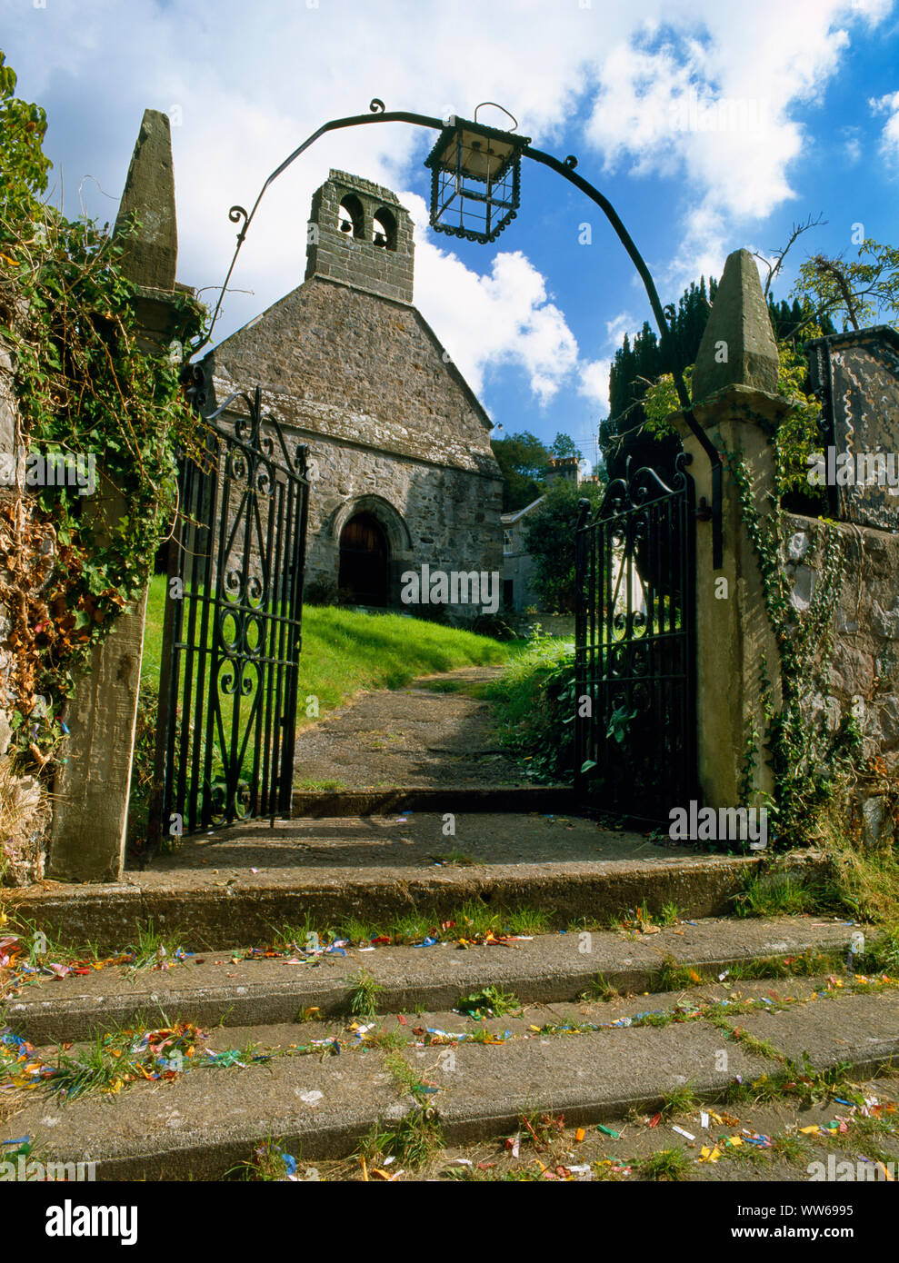 NW principale di ingresso del Cwm chiesa medievale, il Galles del Nord, Regno Unito, con passi dalla strada, arenaria gatepiers, ferro overarch & electric lanterna. Foto Stock