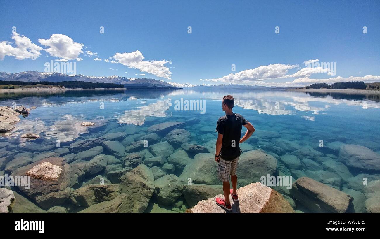 L uomo sta di fronte acqua cristallina con la montagna innevata all'orizzonte, Nuova Zelanda Foto Stock
