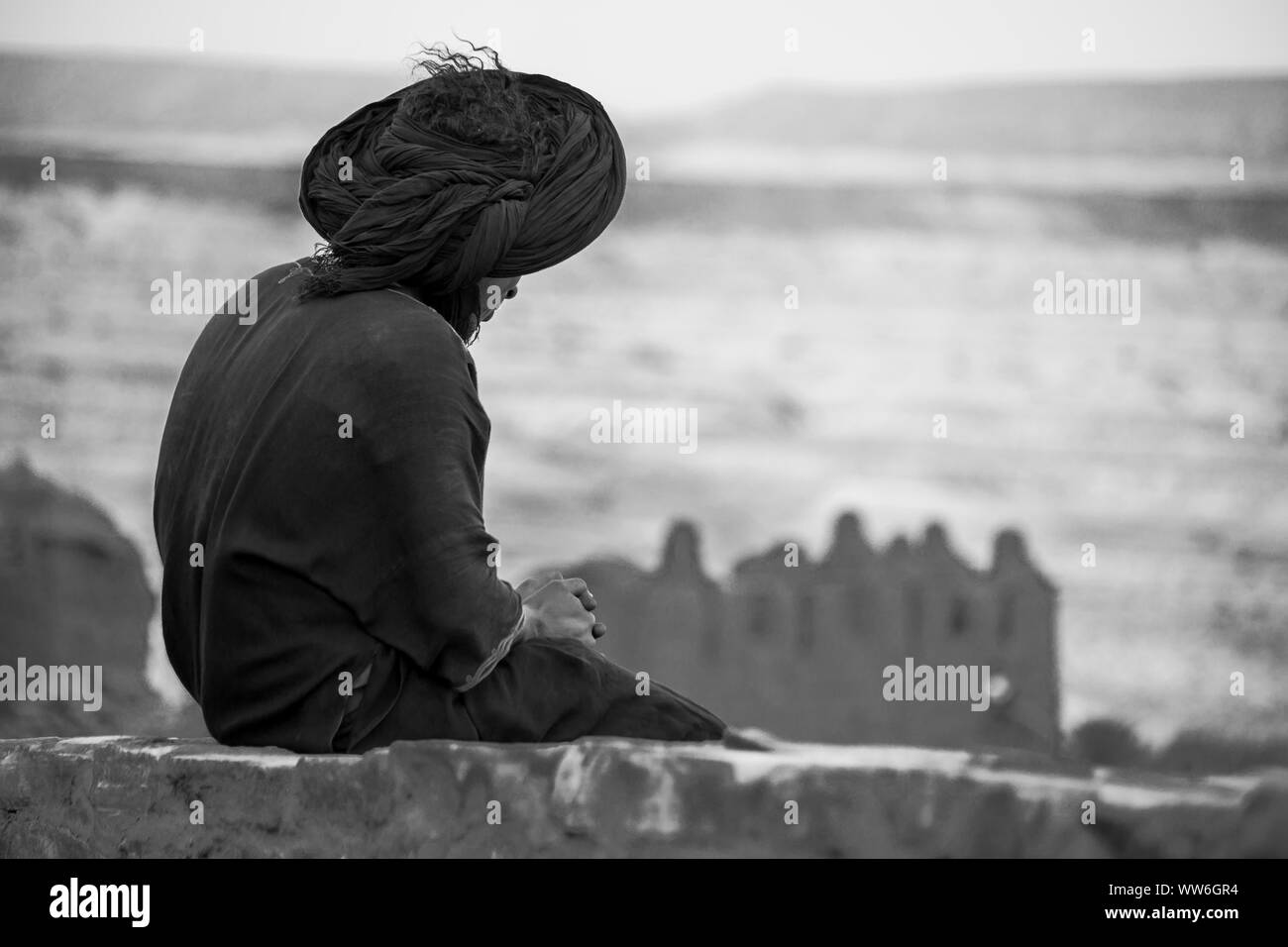 Il Marocco, montagne Atlas, Ait Ben Haddou, uomo seduto su un muro di mattoni Foto Stock