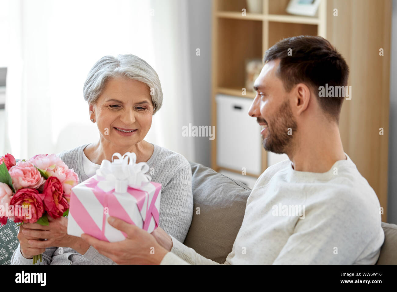 Figlio dando presente e fiori di madre senior Foto Stock