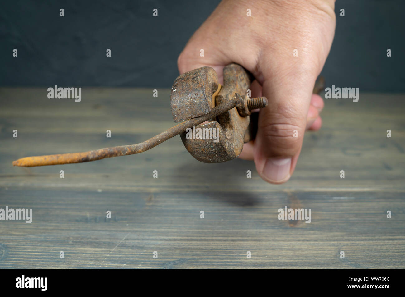 Maschio di mano che tiene il vecchio arrugginito impugnature e piegato lungo corroso chiodo su una tavola in legno rustico in una vista ravvicinata Foto Stock