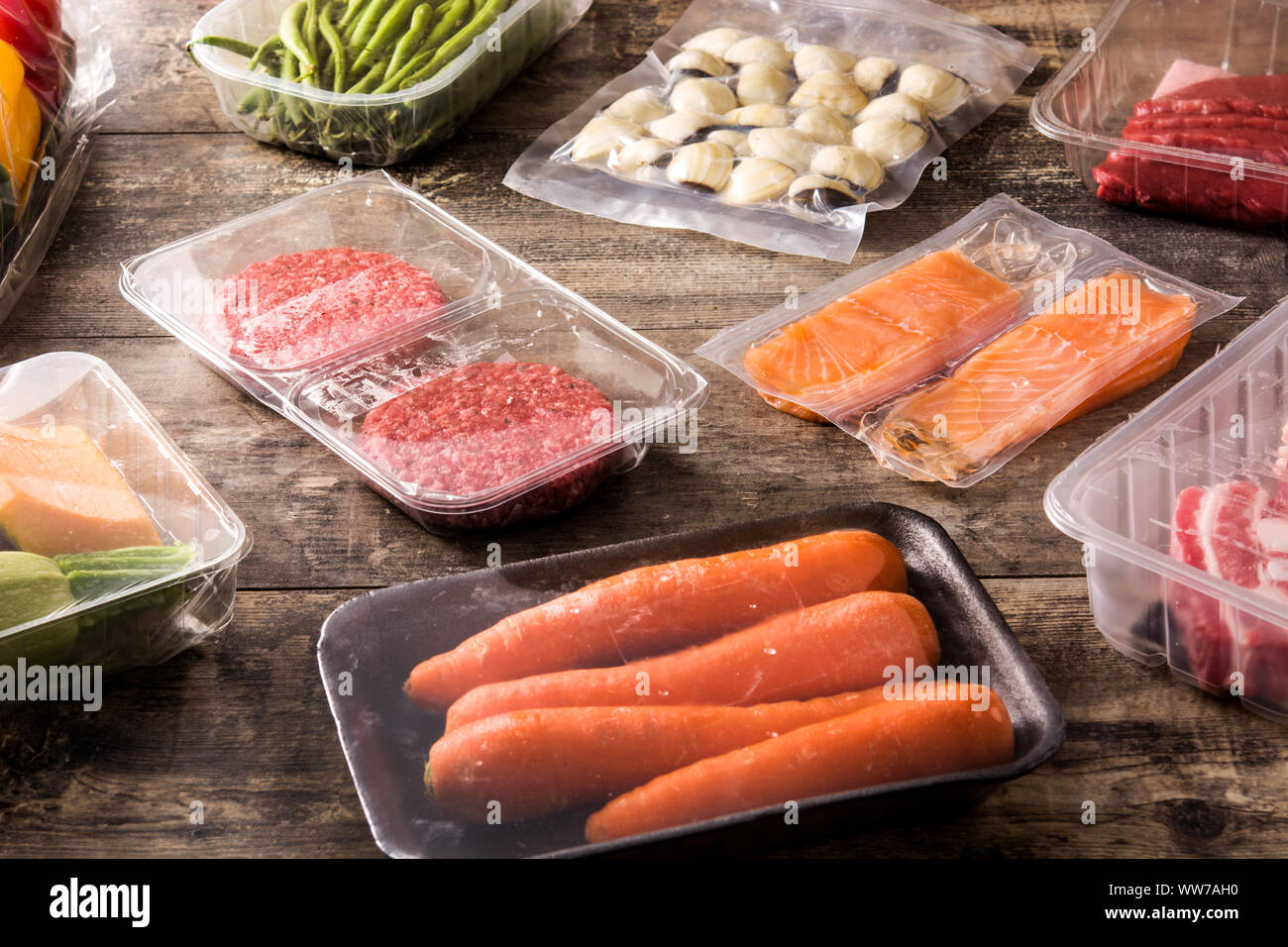 Diversi tipi di alimenti confezionati. Carne, fagiolini, carote e salmone sul tavolo di legno Foto Stock