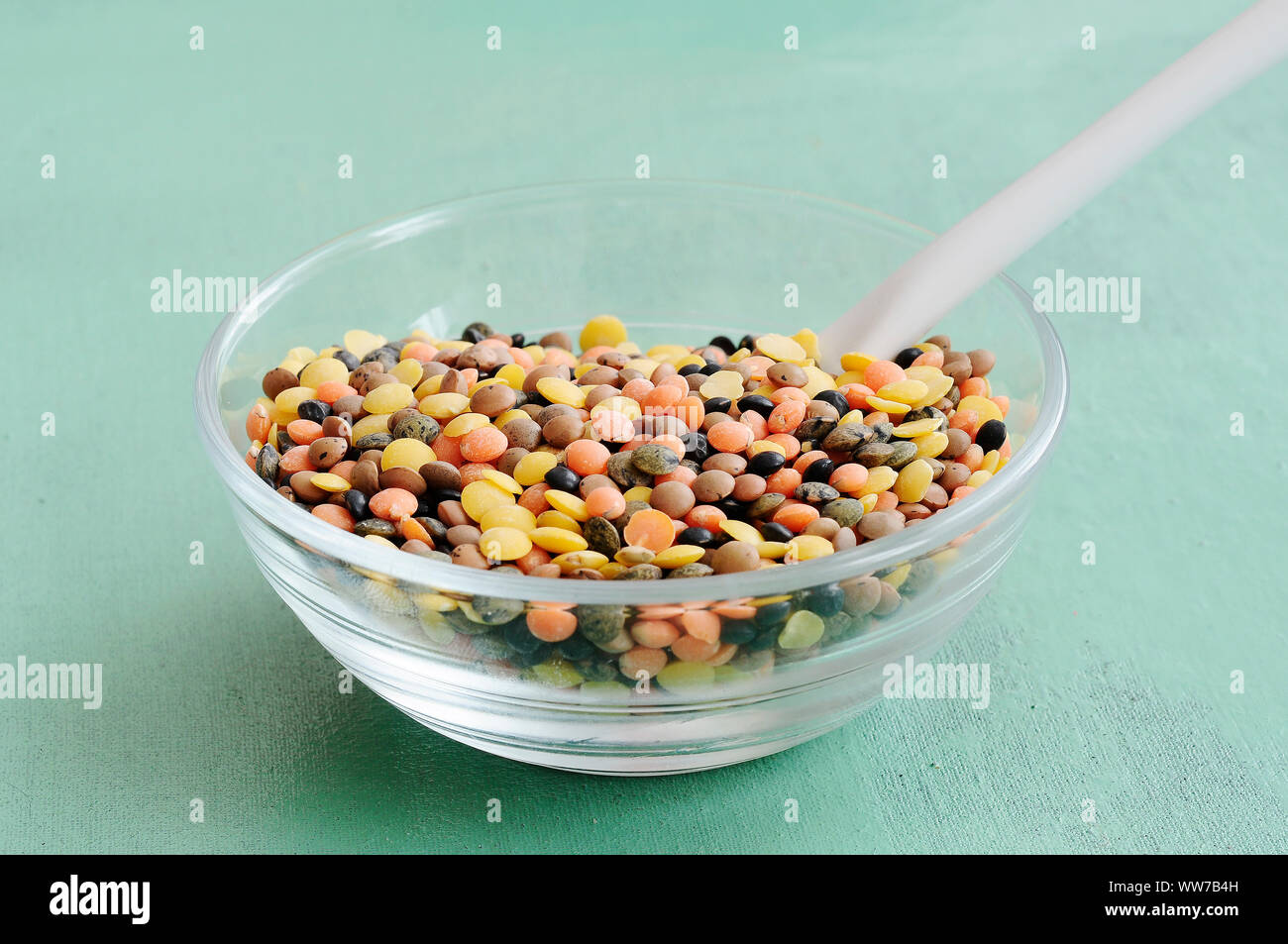 Lenticchie, ciotola di vetro di lenticchie, vari colori, sfondo verde, legumi Foto Stock
