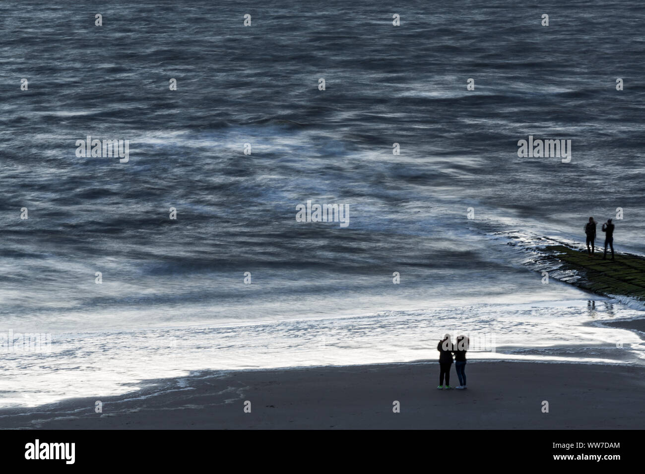 Norderney, Weststrand, Strand, zwei junge Frauen, Meer, in Wellen, Belgium.Wellen, Bewegung, blaue Stunde, Langzeitbelichtung Foto Stock