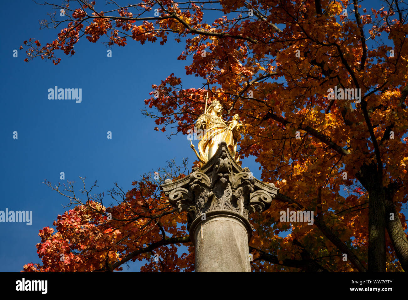 Una statua dorata della Vergine Maria sotto il cielo blu in autunno a basso angolo di visione Foto Stock