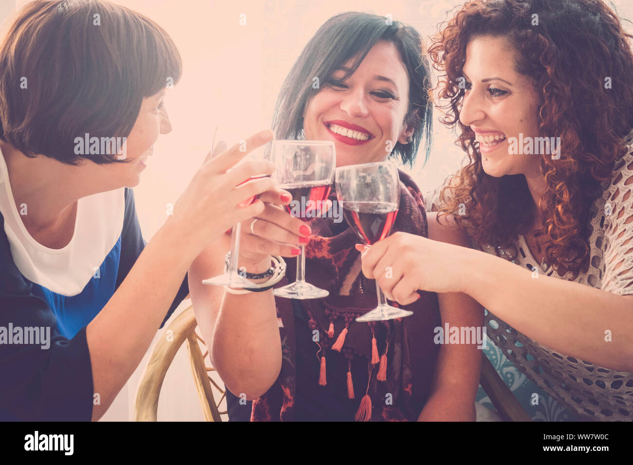 Gruppo di persone a tre giovani donne di bere un po' di vino rosso a casa per celebrare la loro amicizia. Molto divertente e faccine per un giorno di festa Foto Stock