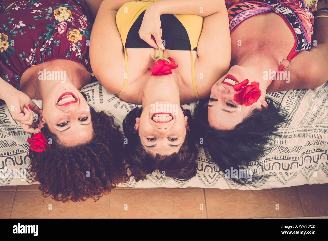Bella bella e tre donne caucasici a casa. stabiliscono sul letto guardando in alto con un grande sorriso e felicità. giocando con le rose e i colori rosso rossetto e fiori. felicità amicizia Concetto di immagine Foto Stock