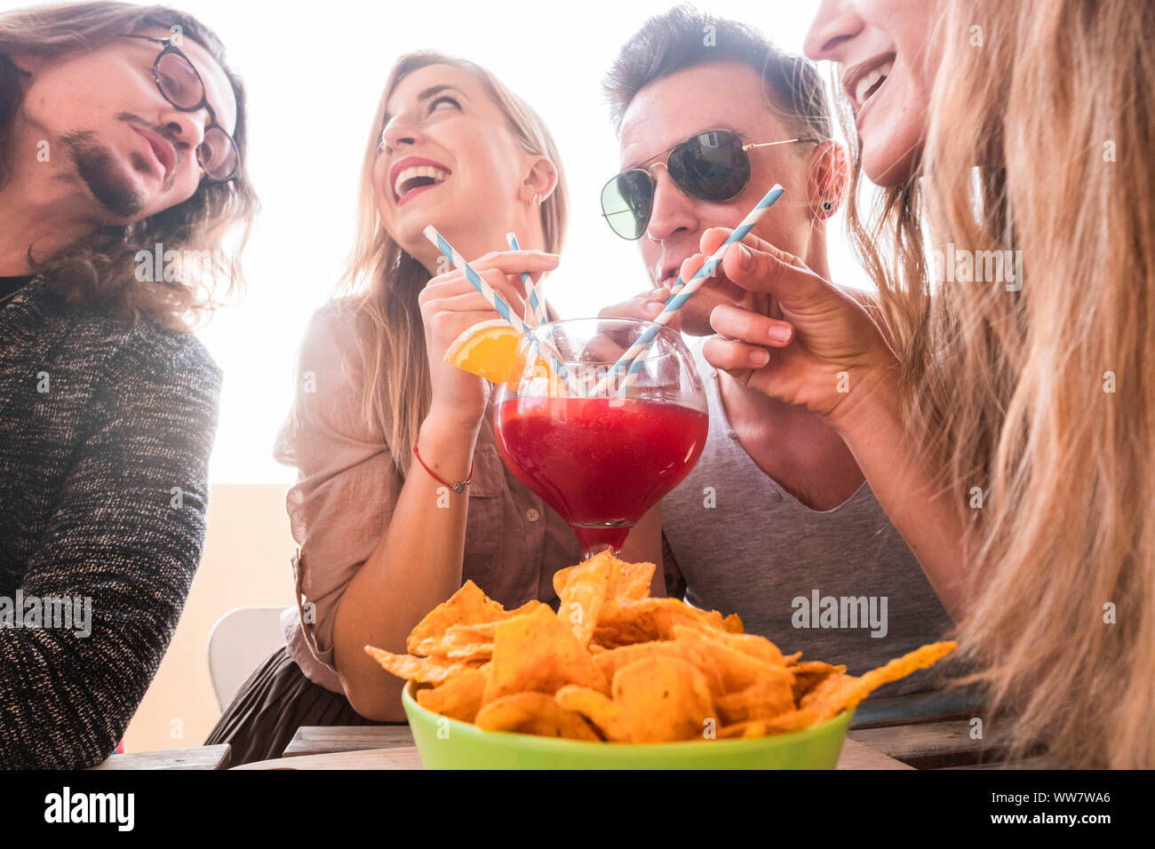 Quattro uomini e donne hanno divertimento insieme amicizia bere tutti con lo stesso vasetto in vetro con arancia rossa frutta. tempo di festa con fondo trasparente per i giovani Foto Stock