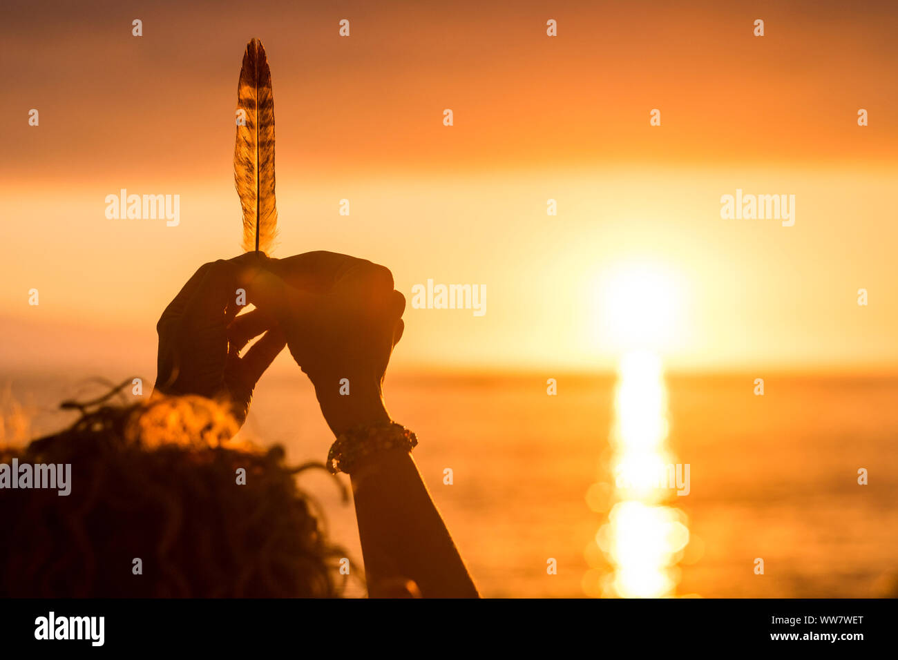 Donna mani prendendo una piuma di fronte a una straordinaria golden e caldo tramonto sul mare. vacanza libertà e indipendenza concetto. per godersi la natura e con la sensazione che il mondo. immagine concettuale con il peso e la vita Foto Stock