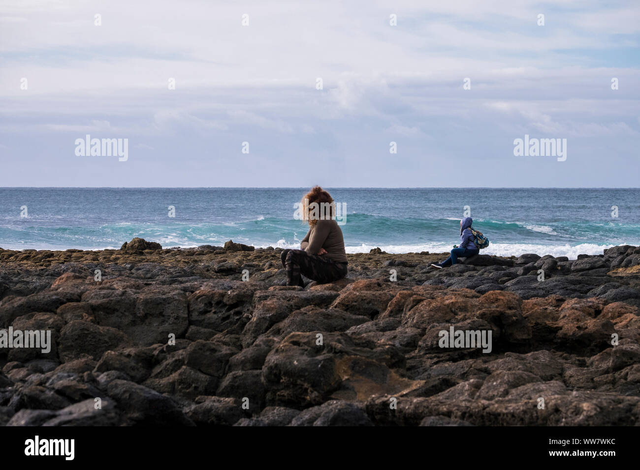 Una donna e un uomo sedersi guardando la potenza dell'oceano durante una stagione fredda come in inverno Foto Stock