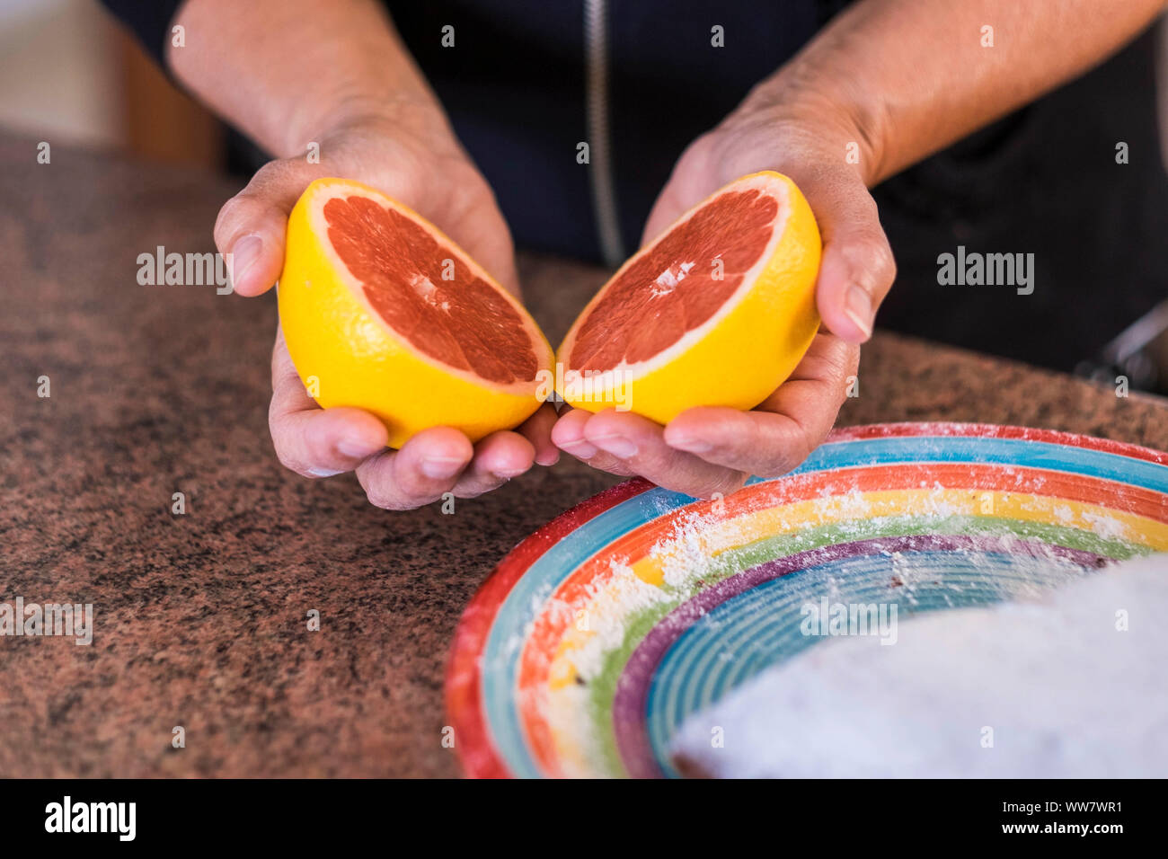 Il cibo fresco frutta colorata di pompelmo, aperto a metà presi con le mani sul tavolo pronti a mangiare i prodotti di stagione da terra. Uno stile di vita sano Foto Stock