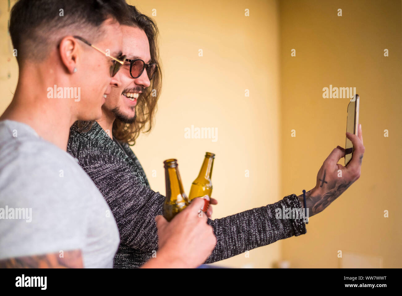 Bella uomini caucasici giovane guardare il telefono cellulare per scattare foto. birra e divertimento all'aperto sorridente concentrarsi sul secondo uomo. toatto e concetto alla moda Foto Stock