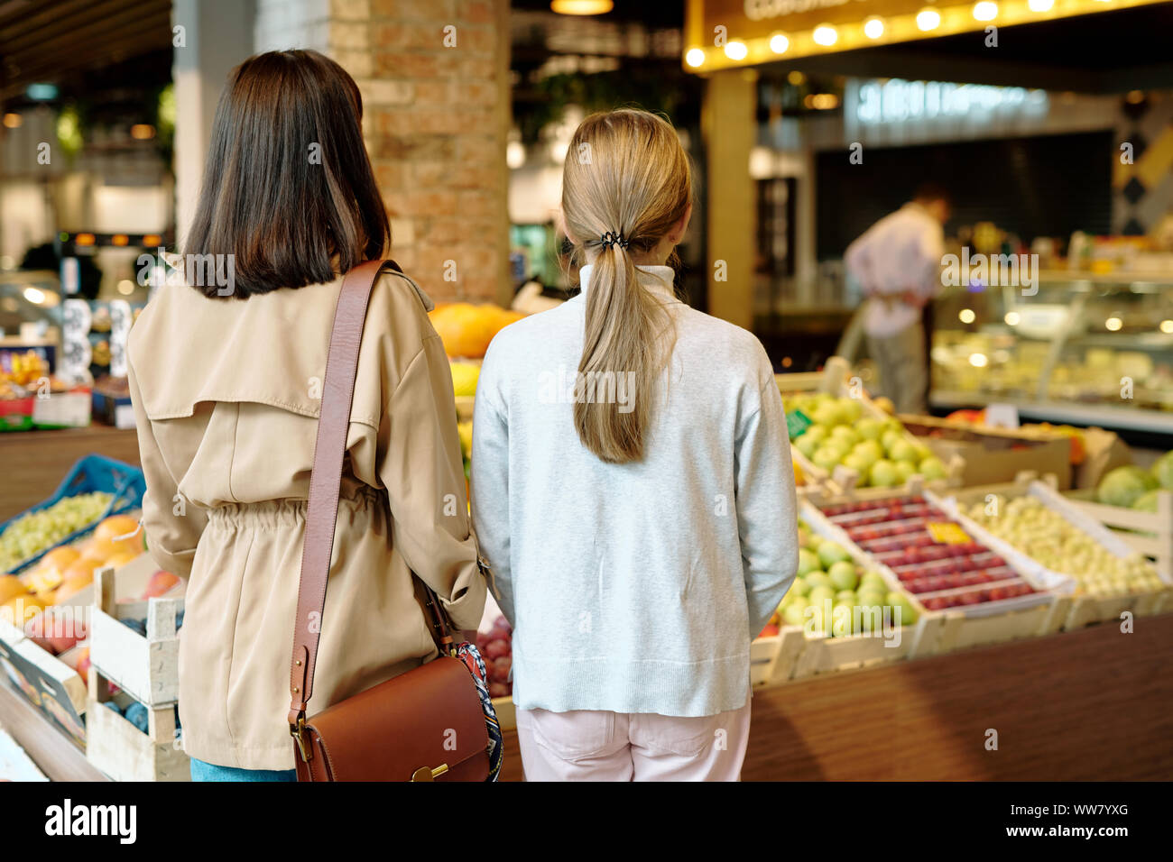 Vista posteriore della giovane donna e sua figlia in piedi da display con frutta fresca Foto Stock