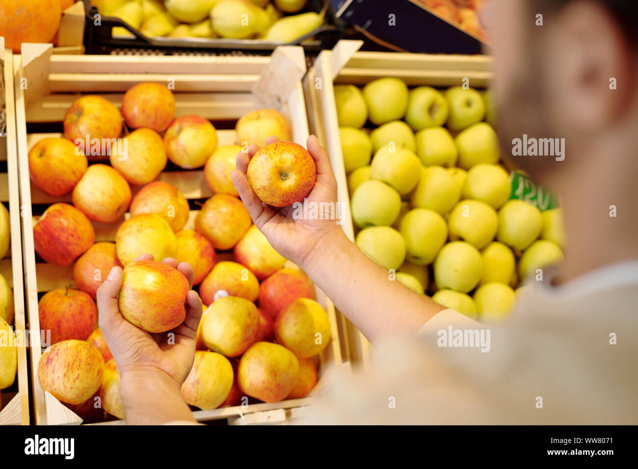 Giovane uomo scegliendo fresche e mature mele di colore giallo mentre in piedi dal display di frutta Foto Stock