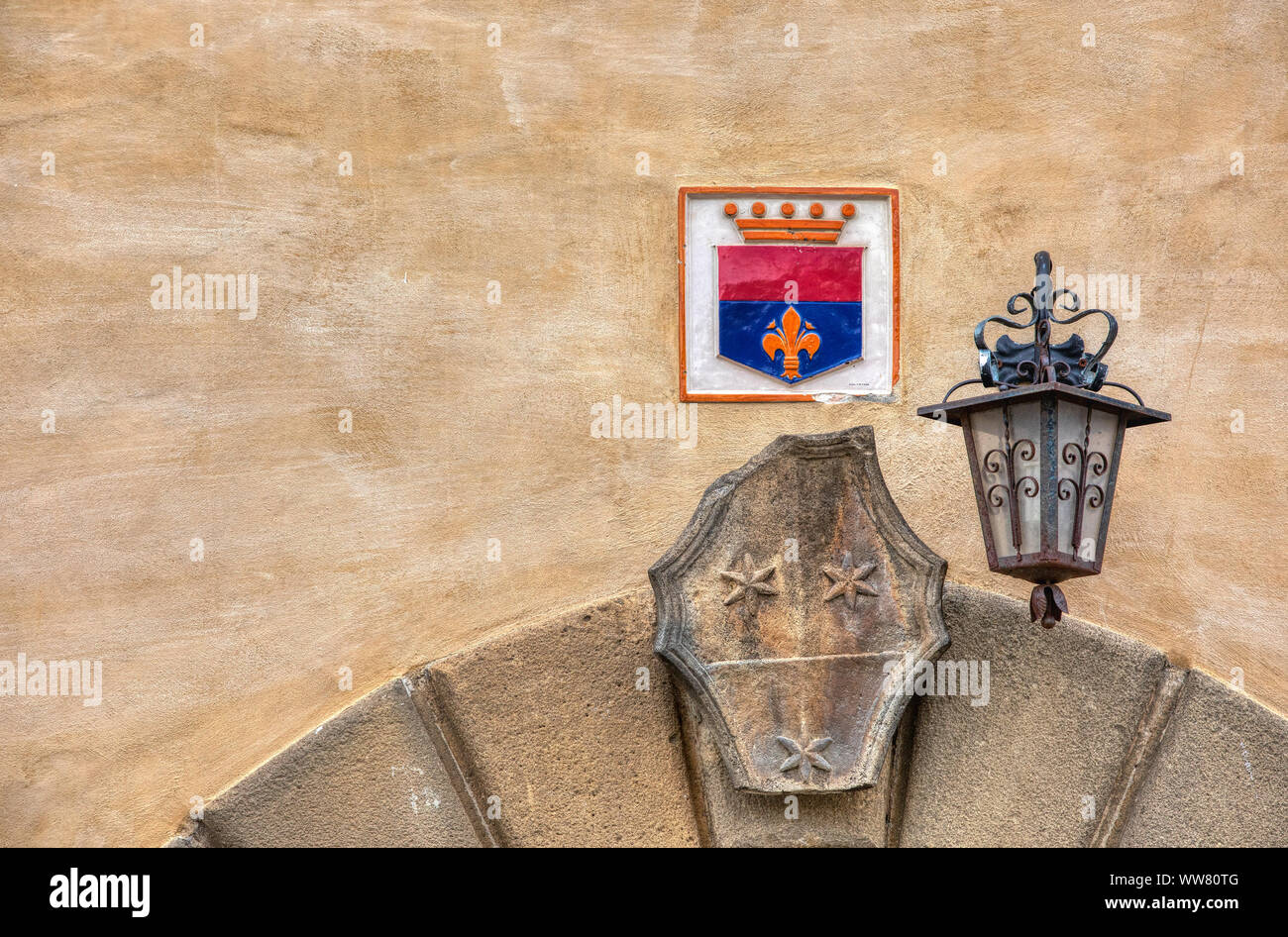 Fotografia di una porta di monumenti medievali archway con un colorato stemma di famiglia e un weathered nero ferro battuto street light. Foto Stock