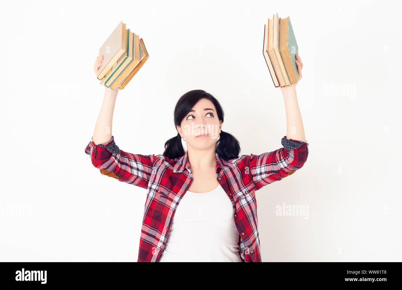 Una studentessa in una camicia rossa di plaid tiene la pila dei libri alla parte superiore in ogni mano. Preparazione all'ammissione all'università, alla sessione o agli esami. Foto Stock