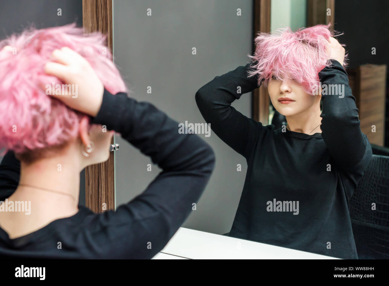 Bella acconciatura di giovane donna guardando nello specchio dopo la morte dei capelli e rendendo mette in evidenza in un salone di bellezza. Vicino a breve taglio di capelli rosa Foto Stock