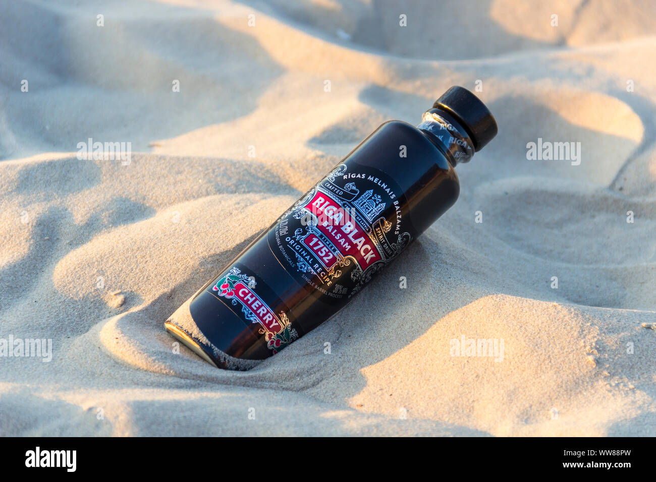 JURMALA, Lettonia - 1 Settembre 2019: Bottiglia del famoso lettone liquore a base di erbe Riga Black Balsam Cherry recante nella sabbia sulla spiaggia di Jurmala Foto Stock