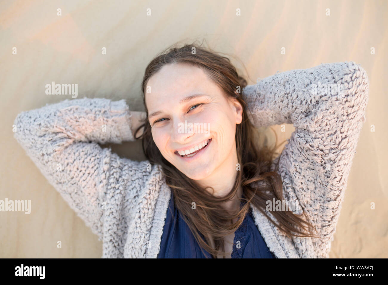 Giovane donna che giace nella sabbia e sorridente Foto Stock