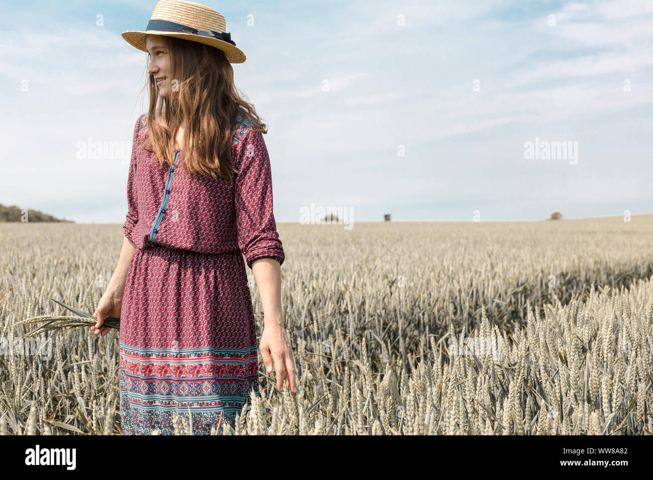 Giovane donna in abiti estivi e con cappello di paglia sul campo di grano Foto Stock