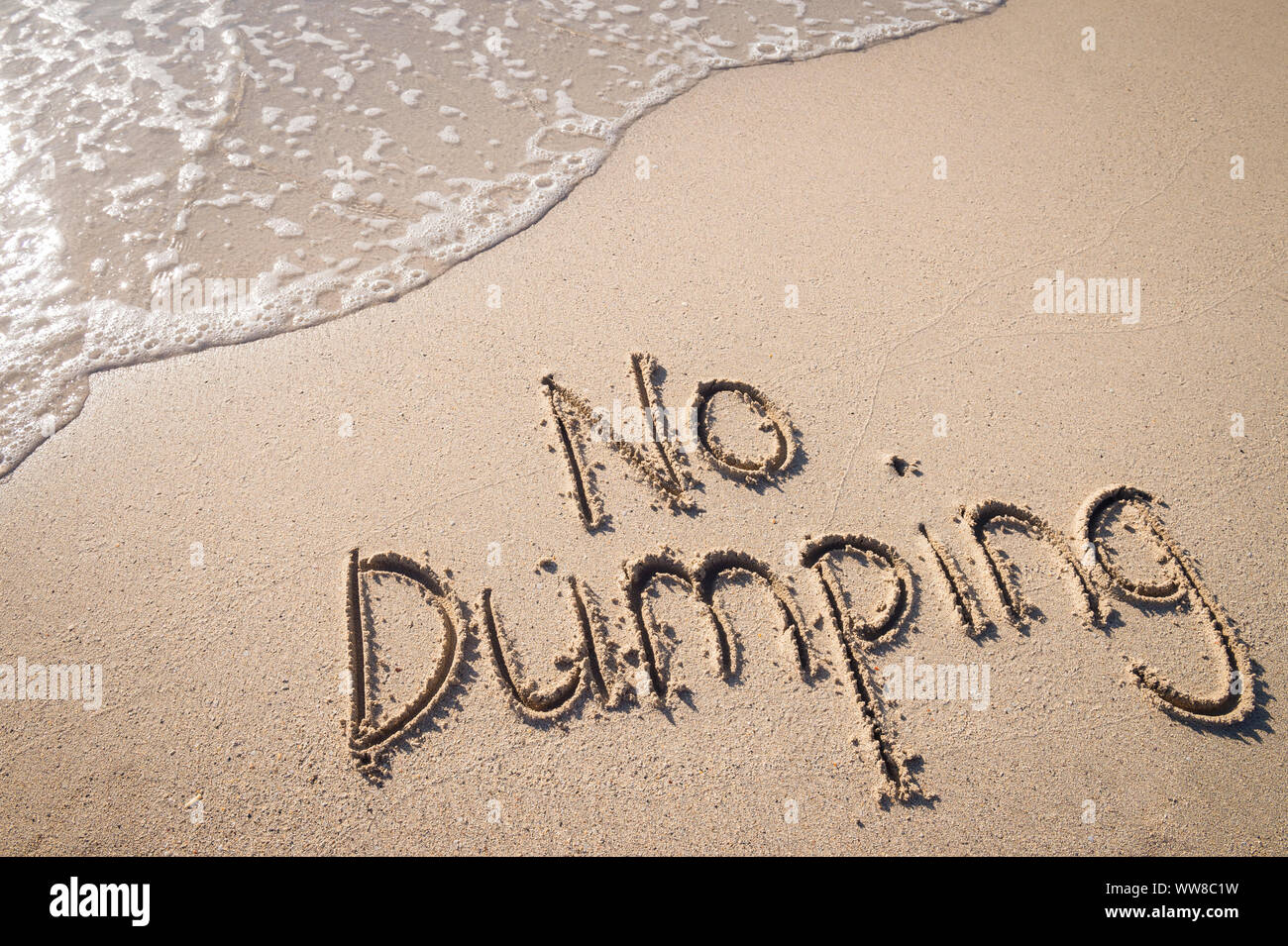 Nessun Dumping oceano messaggio inquinamento scritti a mano in testo semplice in liscia spiaggia di sabbia con onda in arrivo Foto Stock