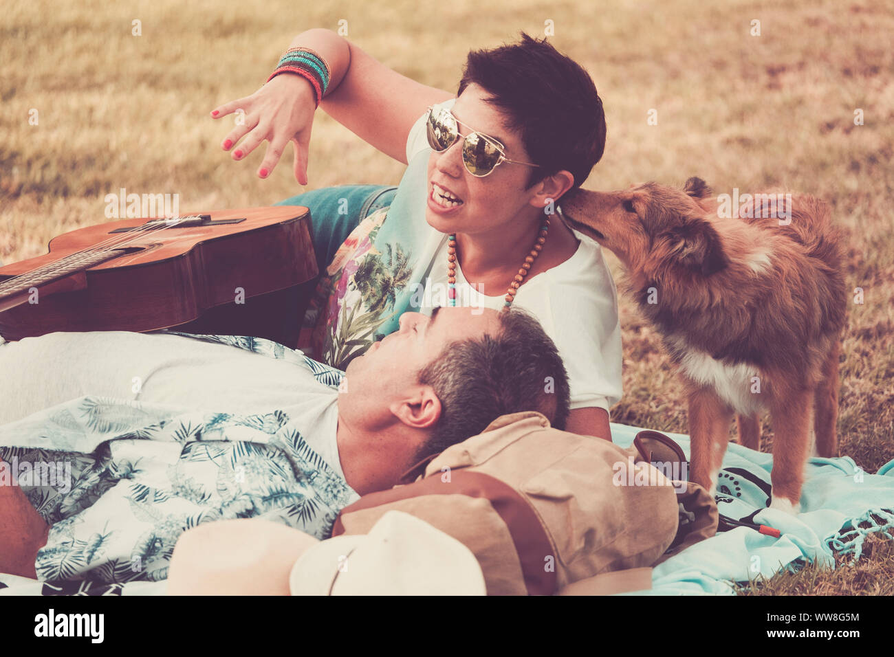 Romantico vintage in scena con la giovane bella donna e uomo stabilisce sull'erba godendo il giorno, poco giovane animale shetland baciarla, hippy e pacifica il concetto di amore e di musica con la chitarra Foto Stock