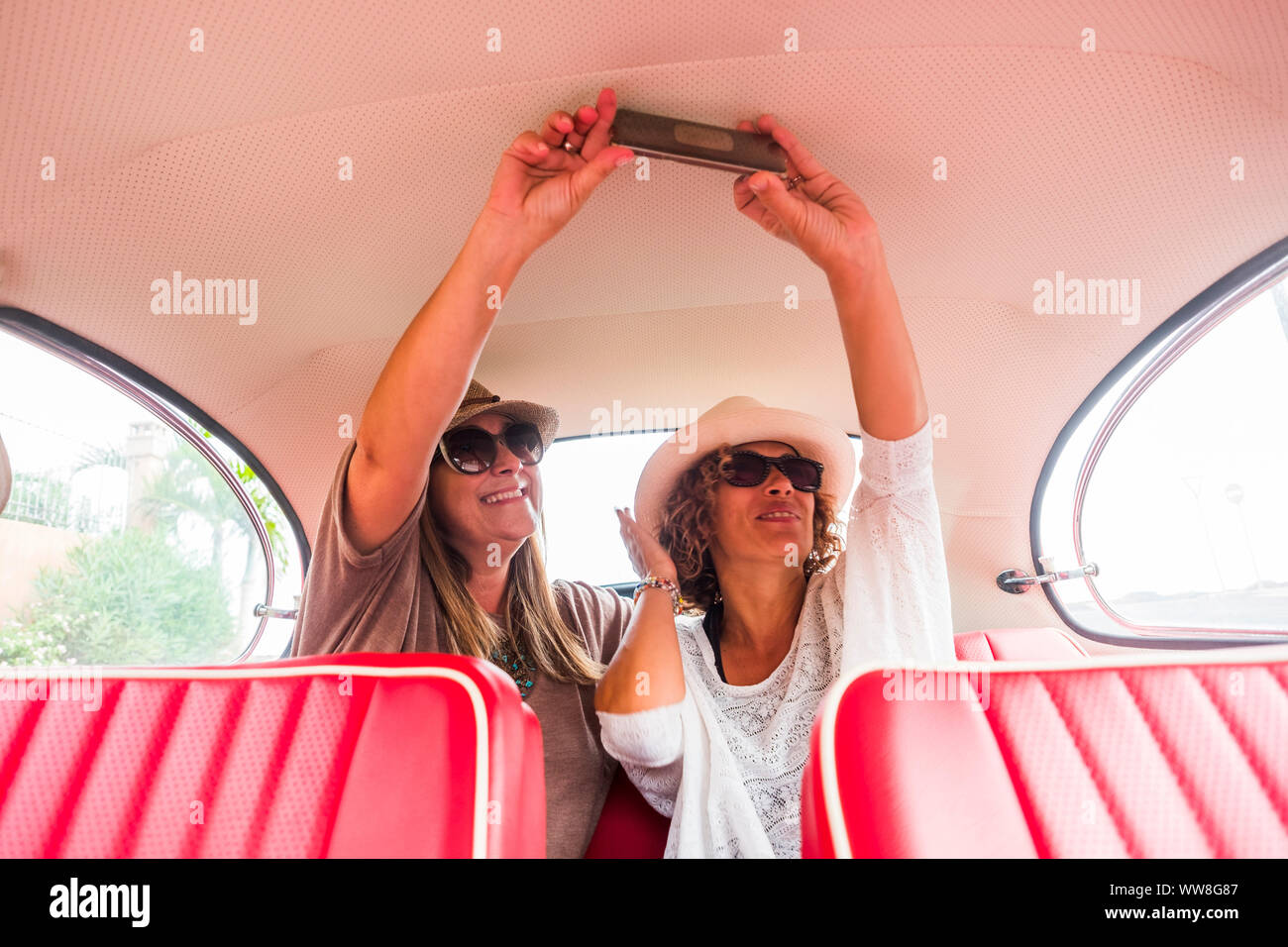 Coppia di donne caucasian gli amici sorseggiando un rosso auto d'epoca, tenendo selfie con un moderno smartphone, contrasto od cose nuove tecnologie correlate Foto Stock