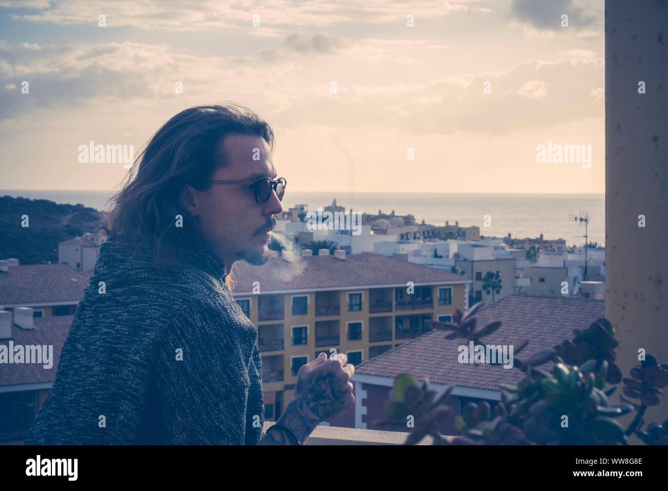Grave bellissimo modello da uomo stare fuori in terrazza a casa con bella vista di case e città e dell'oceano orizzonte, il tramonto nella notte estiva, fumatori e rimanere solo concetto Foto Stock