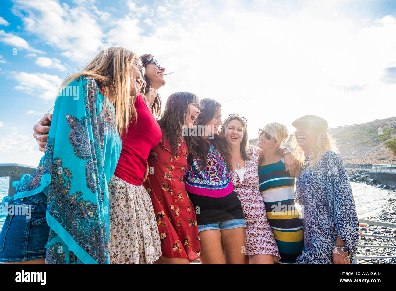 Il gruppo di sette bello e belle ragazze caucasici giovani donne di divertirsi e ridere e sorrisi per esterno in prossimità dell'oceano durante il tramonto, retroilluminazione persone godendo il tempo libero attività insieme Foto Stock