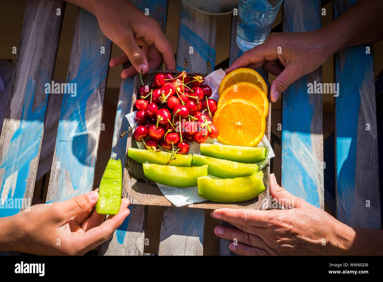 Close up di giovani e vecchie mani da nonna e adolescente nipote di mangiare alcuni freschi frutti di stagione sulla tavola di legno, uno stile di vita sano in famiglia all'aperto, luci e ombre Foto Stock