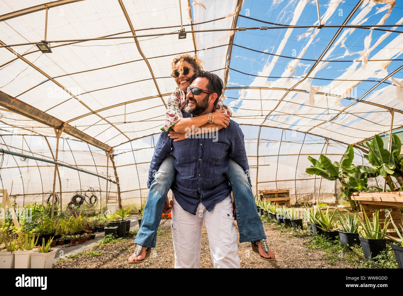 Bella donna con lunghi capelli ricci a cavallo sul retro dell uomo bello in agricoltura posto shop, outdoor persone caucasian divertirsi insieme, sposato e amore concetto sotto un clima soleggiato in luogo biologico Foto Stock