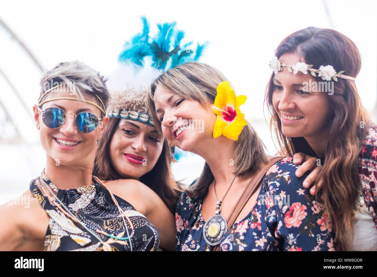 Quattro allegro belle giovani donne festeggiare insieme e prendere una immagine selfie sorridente e divertirsi in amicizia, parte il concetto con abiti colorati e fiori folla, sfondo luminoso, felici le persone Foto Stock