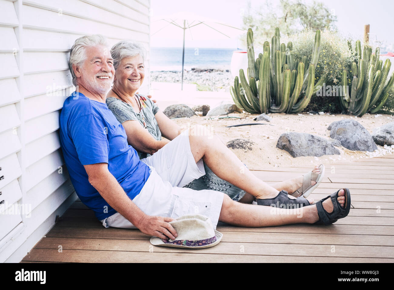 Felice coppia senior di ridere seduti in terra su tavole di legno su un giorno di estate Foto Stock