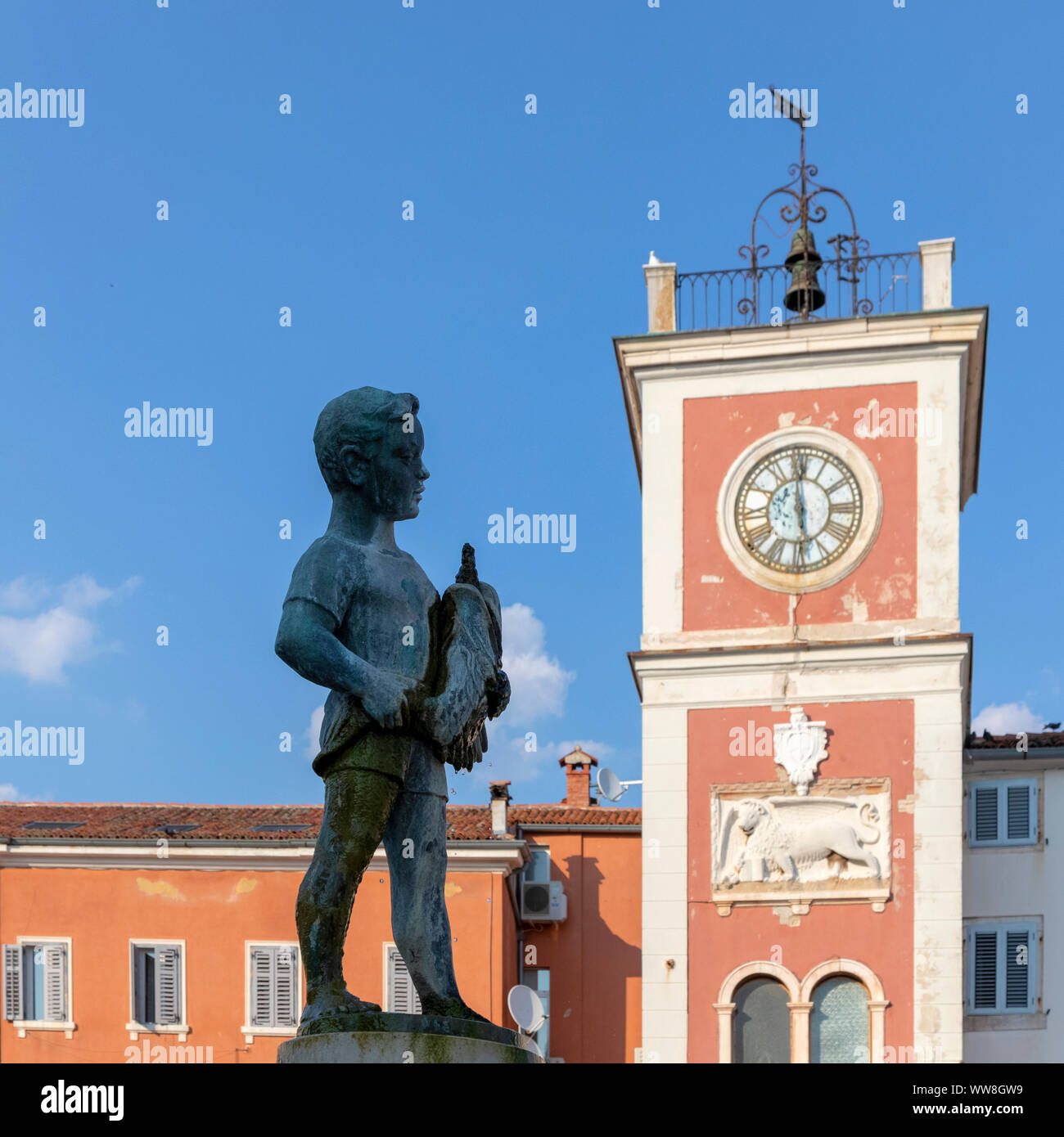 Il ragazzo con la fontana del pesce e il rosso di clock tower in Trg M. Tita, Rovigno, Istria, Croazia Foto Stock