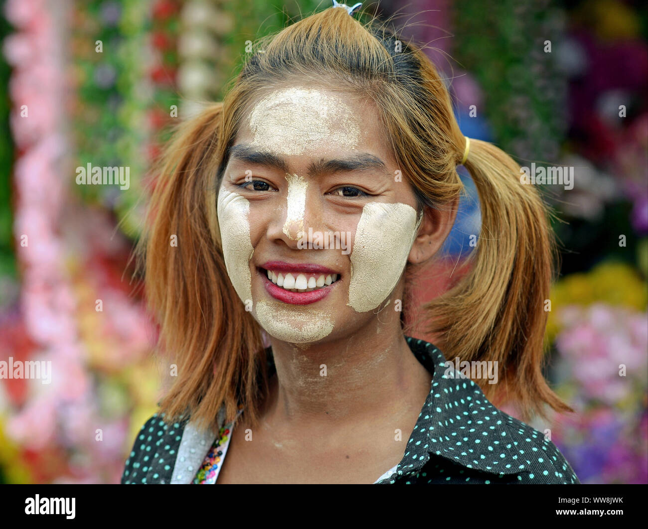 Giovane donna birmana con lunghi pigtail e patch spessa di colore bianco giallastro thanaka tradizionale cosmetica viso tutto il suo volto sorrisi per la fotocamera. Foto Stock