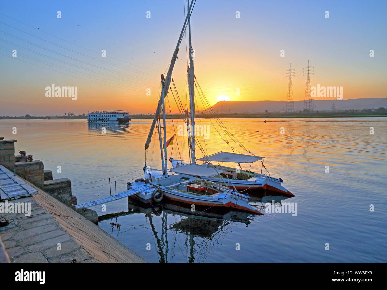 Barche a vela, feluche sulle rive del Nilo con il fiume nave da crociera al tramonto, vicino a Karnak Luxor, Alto Egitto Egitto Foto Stock