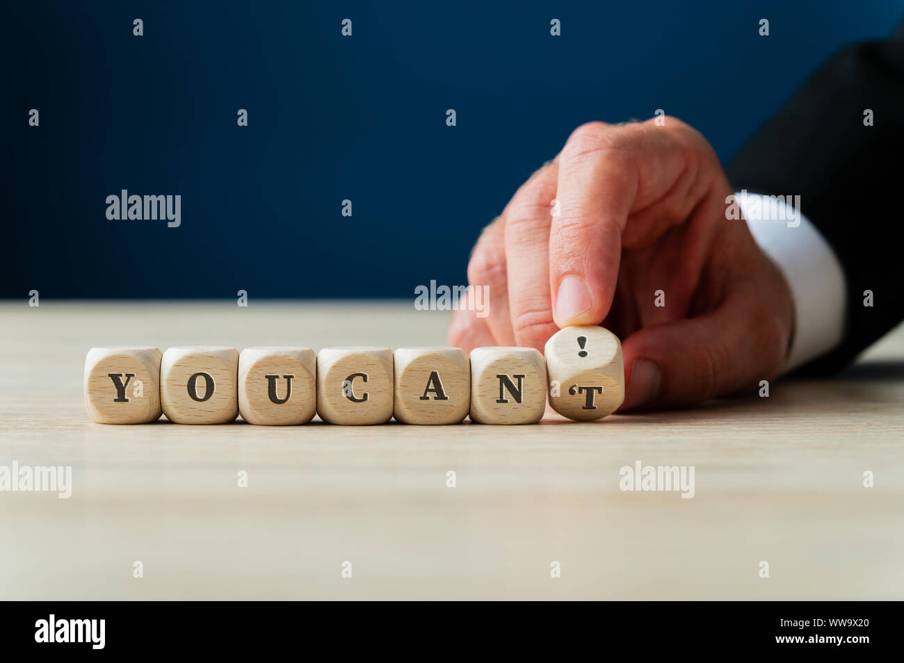 La mano di un imprenditore cambiando un cant segno su cubi di legno in un è possibile! Spostando l'ultimo dado. Foto Stock