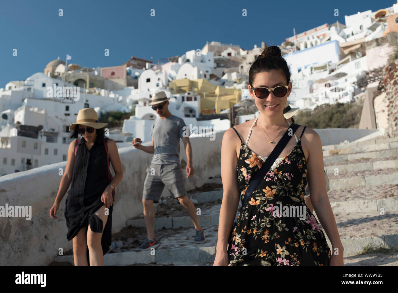 Santorini, Grecia - 24 Giugno 2018: Turisti in cappelli di paglia e occhiali da sole vagare giù pietra passi verso la baia di Ammoudi in Oia, una meta turistica molto destinat Foto Stock