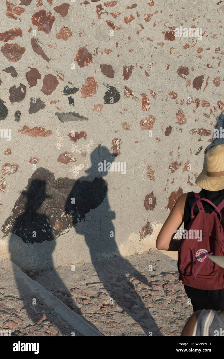 Santorini, Grecia - 24 Giugno 2018: le ombre dei turisti in cappelli di paglia girovagando giù pietra passi verso la baia di Ammoudi in Oia, una meta turistica molto desti Foto Stock