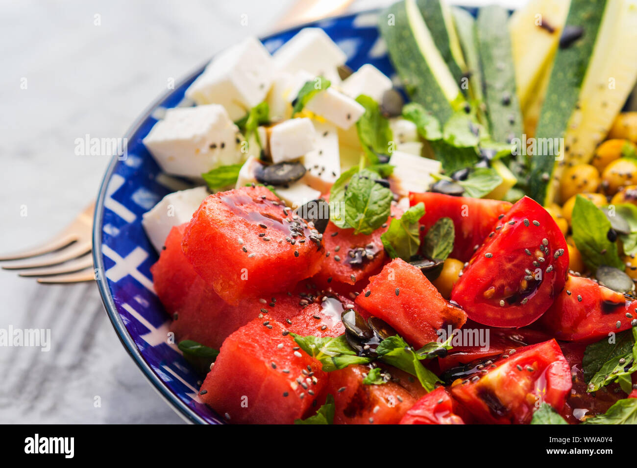 Colorato curcuma anguria di ceci con insalata di formaggio feta, pomodori, zucchine, menta e aceto balsamico sulla tavola di marmo. Estate Fresca facile il pranzo Foto Stock