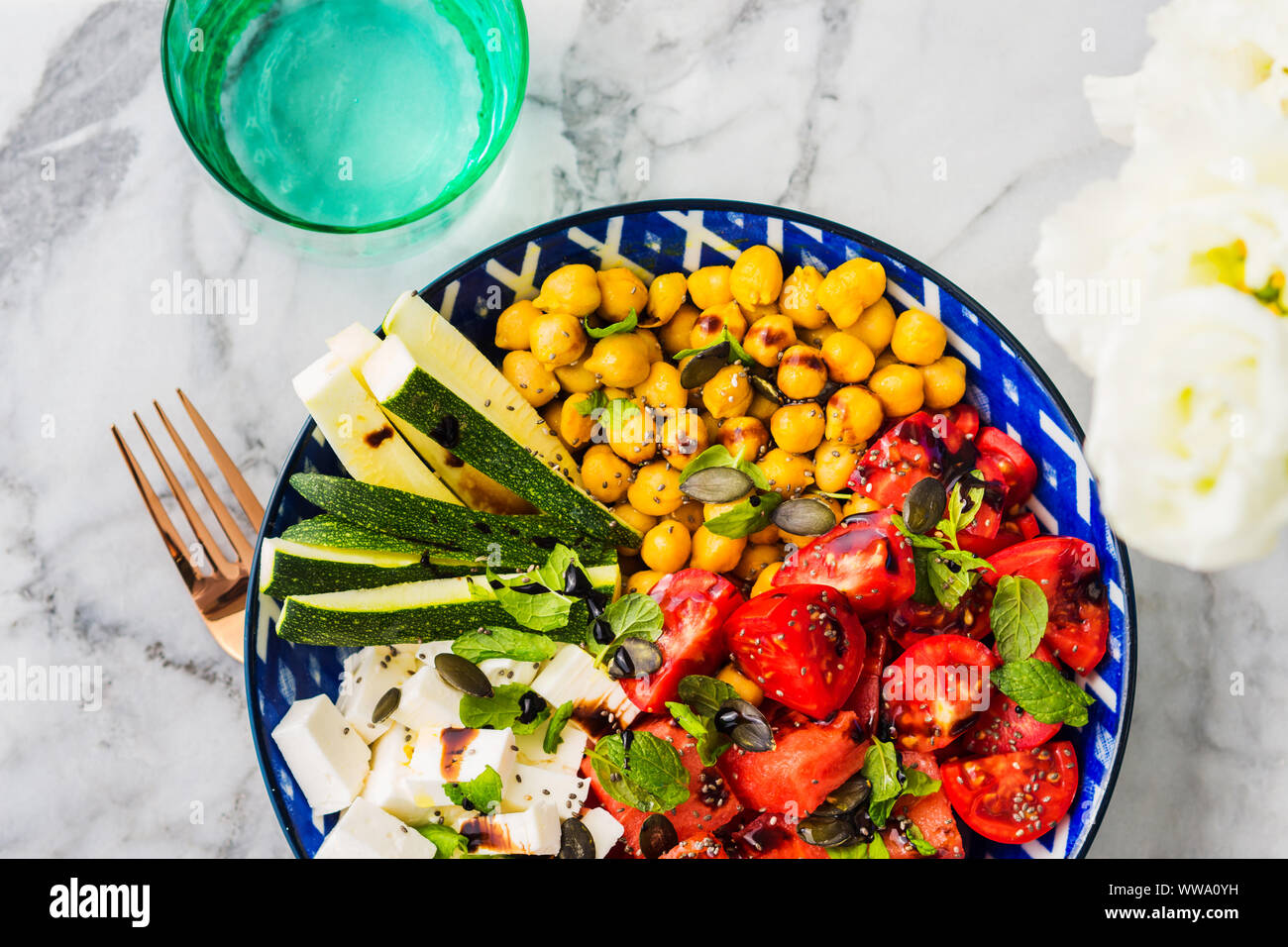 Colorato curcuma anguria di ceci con insalata di formaggio feta, pomodori, zucchine, menta e aceto balsamico sulla tavola di marmo. Estate Fresca facile il pranzo Foto Stock