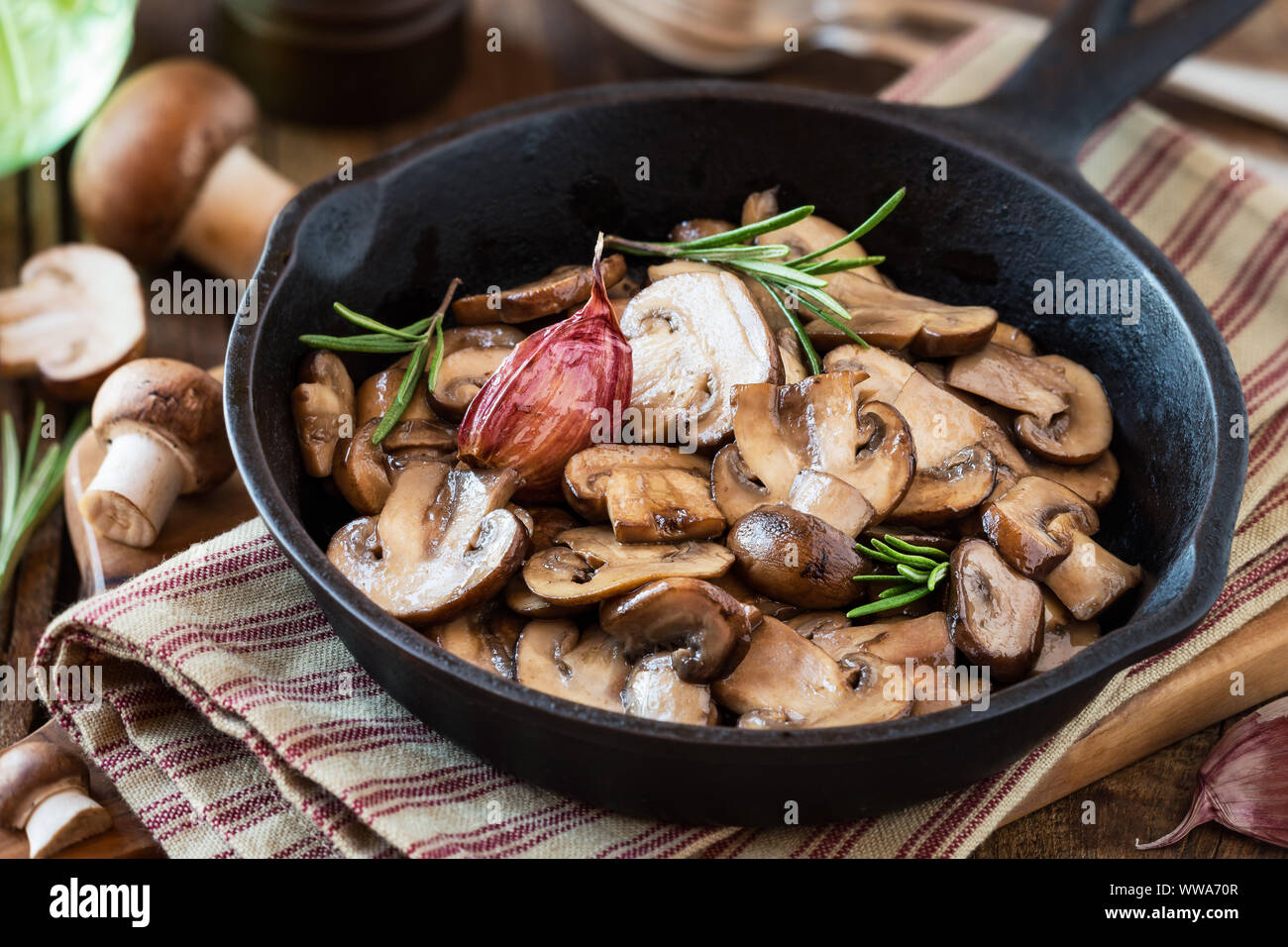 Di castagne cotte funghi o funghi marrone in una padella in ghisa con rosmarino e uno spicchio di aglio viola Foto Stock