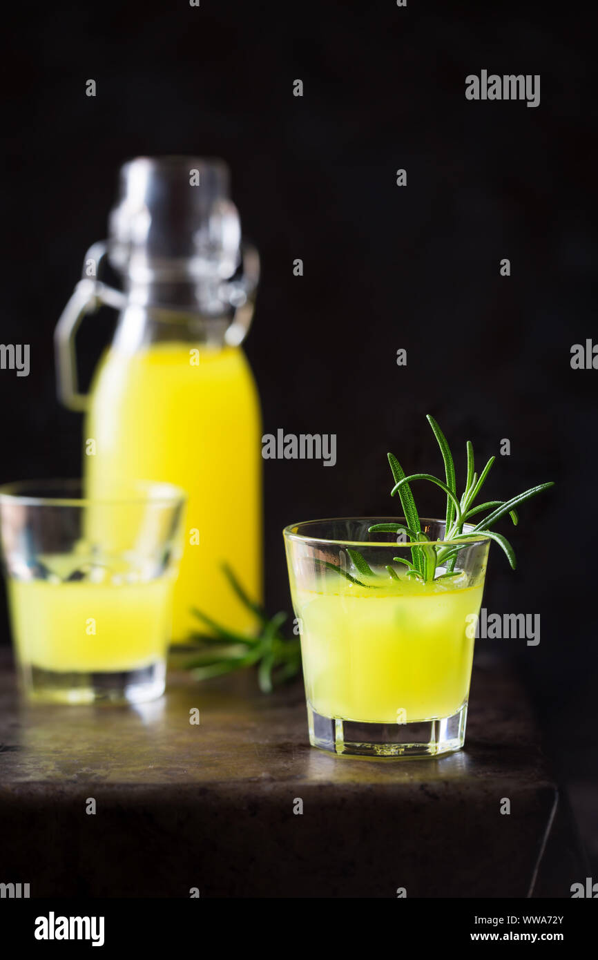 Italiano tradizionale di limone liquore digestivo in un bicchiere servito con un rametto di rosmarino contro uno sfondo scuro Foto Stock