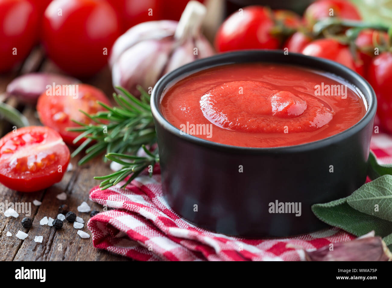 Salsa di pomodoro o ketchup in una ciotola nera con cottura Ingredienti in background Foto Stock