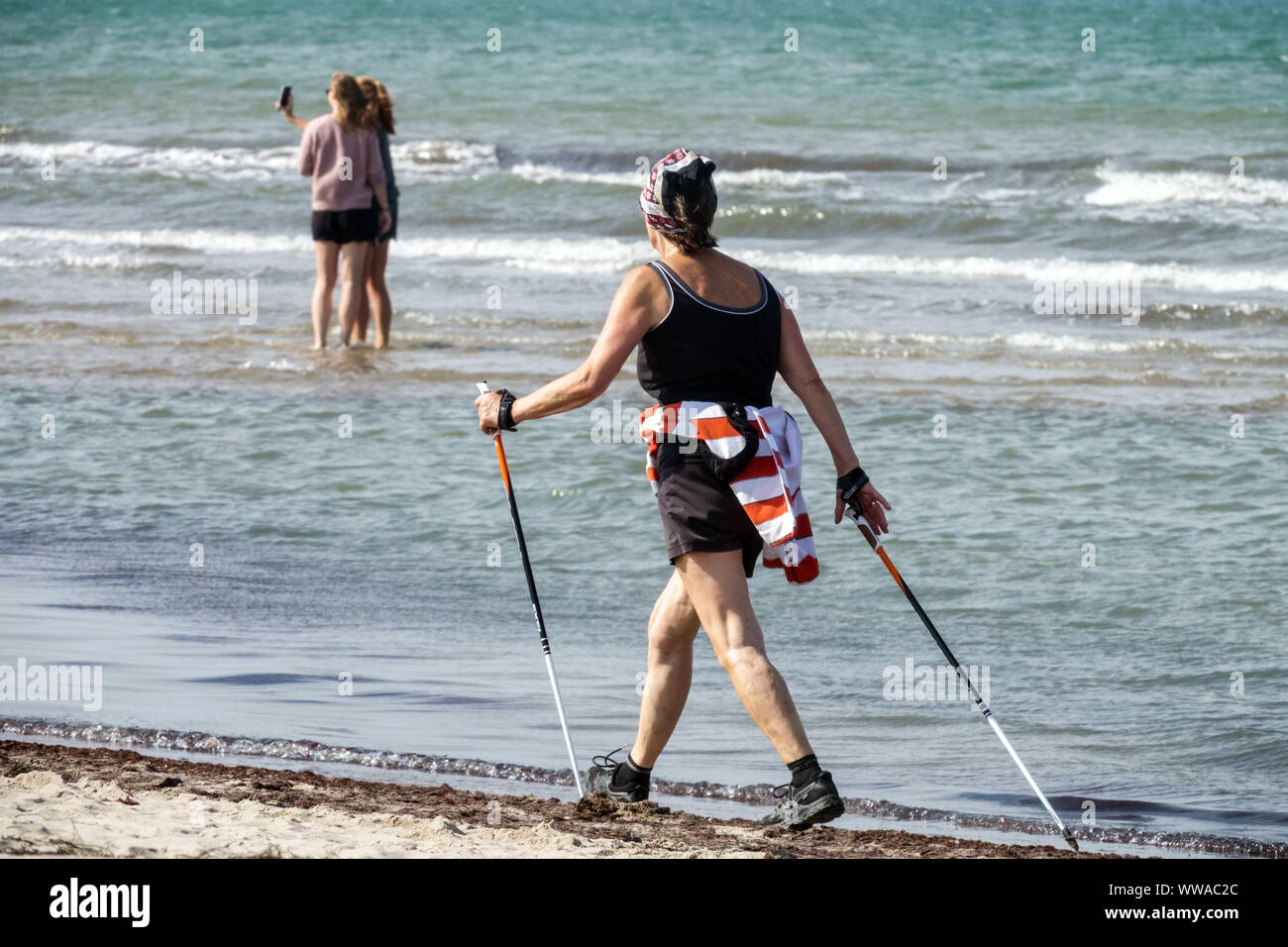 Donna anziana e matura che cammina in nordic walking con i bastoncini lungo la spiaggia del Mar Baltico in Germania Foto Stock