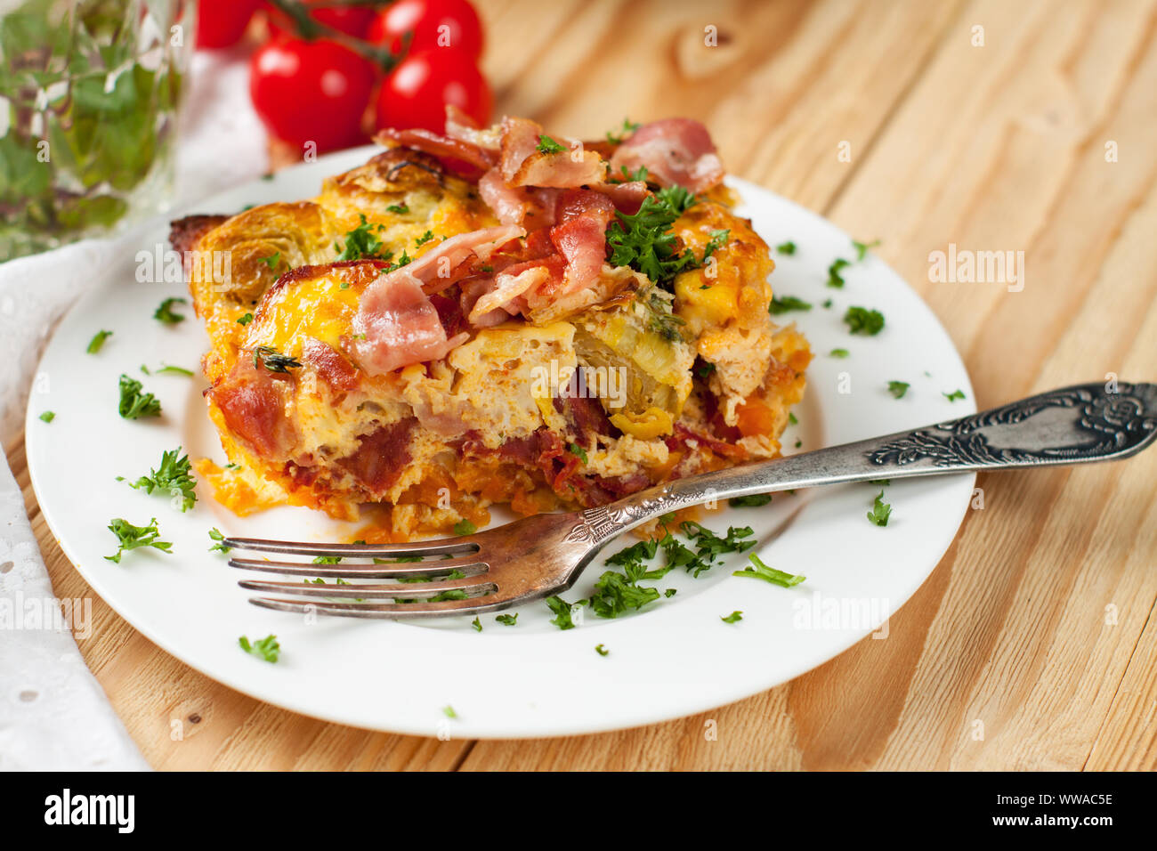 Formaggio al gratin con patate dolci, pancetta, i cavoletti di Bruxelles, uova e pomodori ciliegia sulla luce tavolo in legno Foto Stock